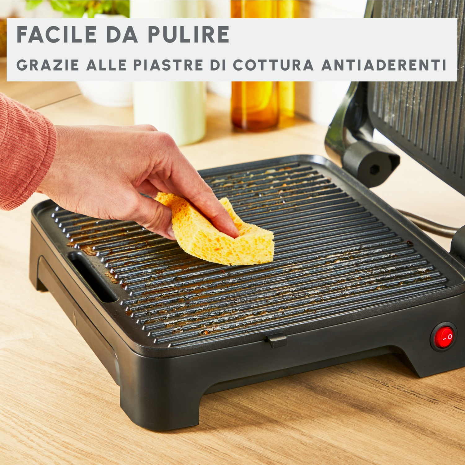 Una mano pulisce le piastre della griglia con una spugna gialla.