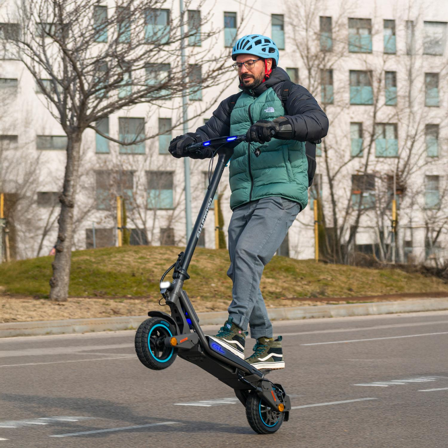 Hombre con casco monta patinete eléctrico a una rueda, chaqueta verde.