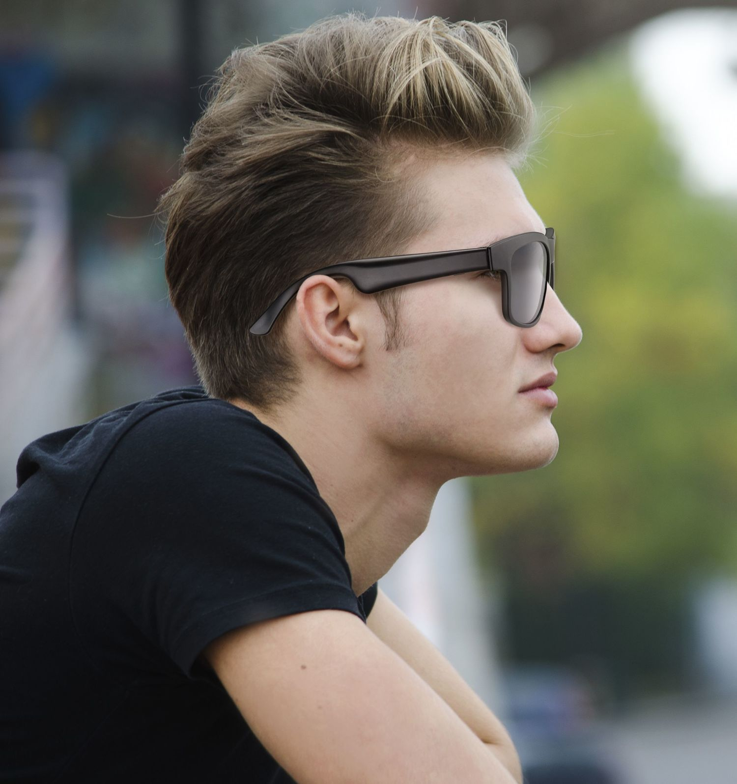Un hombre con cabello rubio y gafas de sol viste una camiseta negra.