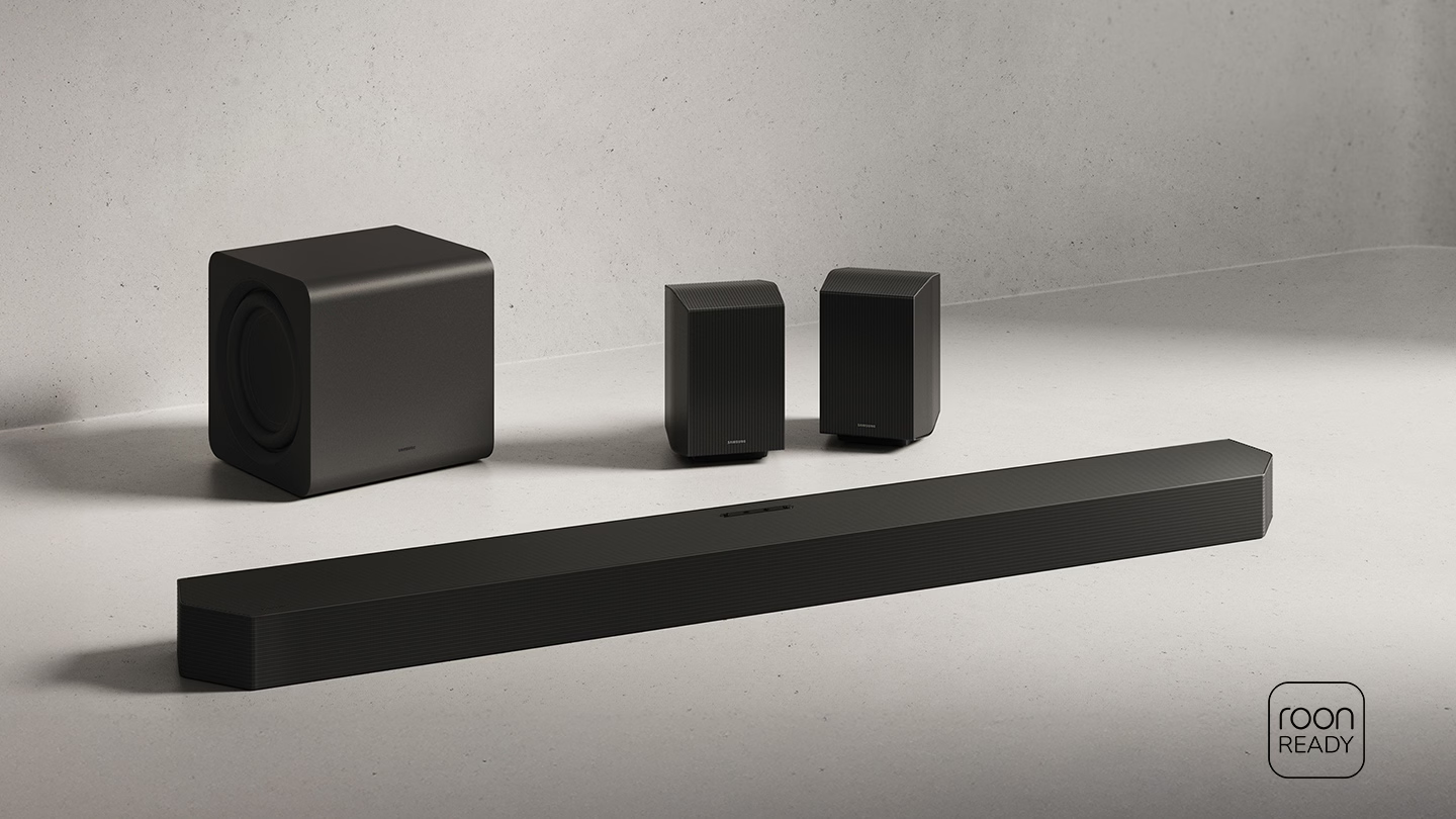 Schwarze Lautsprecher: Subwoofer, Soundbar und zwei Satellitenlautsprecher auf grauem Untergrund.
