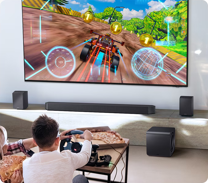 Personen spielen ein Rennspiel auf einem großen Fernseher mit Surround-Lautsprechern.