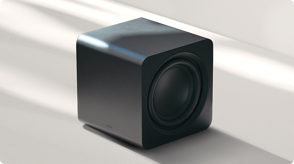 Ein schwarzer Würfel-Subwoofer steht auf einer hellen Fläche mit Schatten.