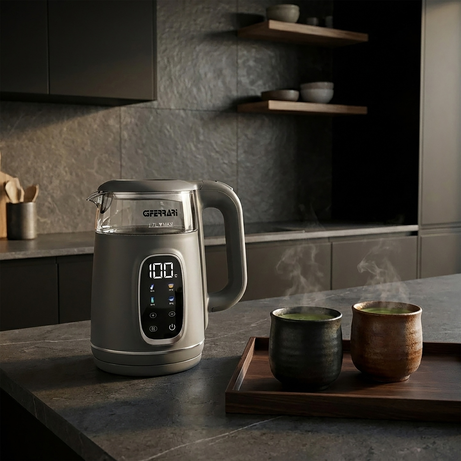 Un bollitore elettrico grigio con display digitale accanto a due tazze fumanti di tè verde.