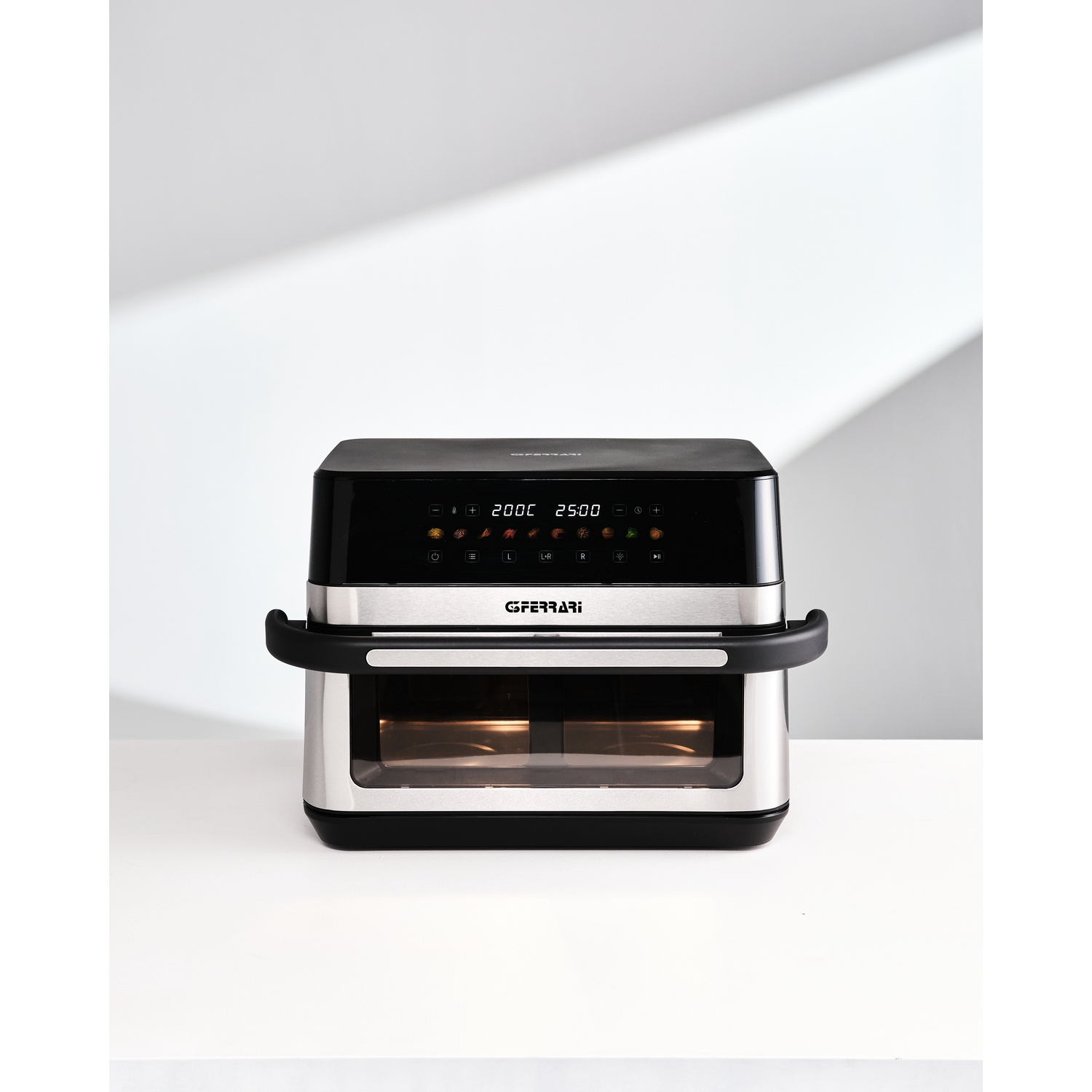 Un forno friggitrice ad aria moderno, nero e argento, con display digitale, su un tavolo bianco.