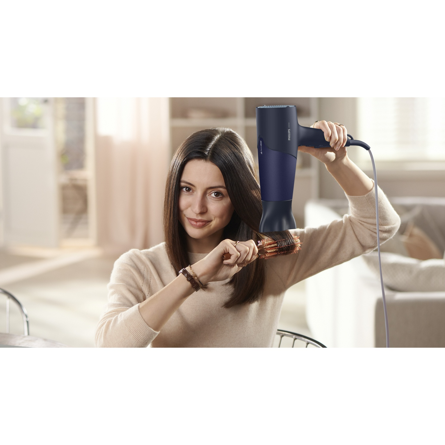 Una donna si asciuga i capelli con un asciugacapelli blu e una spazzola rotonda.