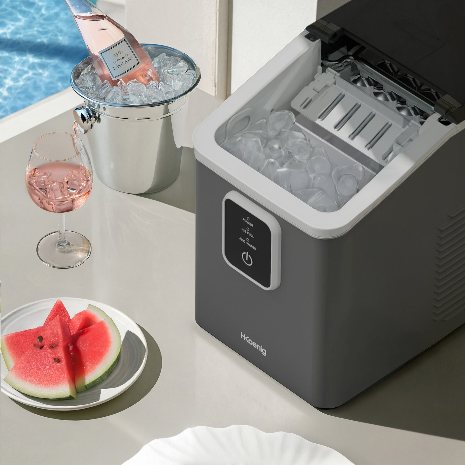 Una macchina del ghiaccio grigia con un bicchiere di rosé, fette di anguria e un secchiello con bottiglia di rosé.