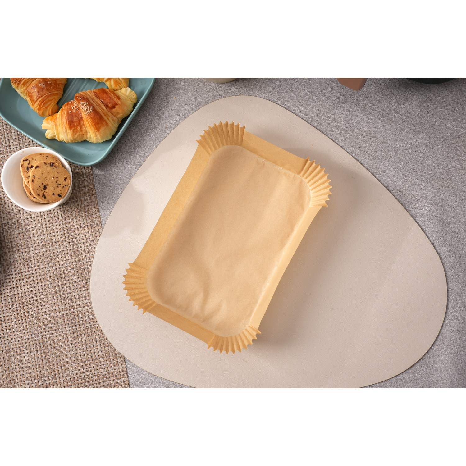 Uno stampo rettangolare in carta da forno su un sottobicchiere, con croissant e biscotti nelle vicinanze.