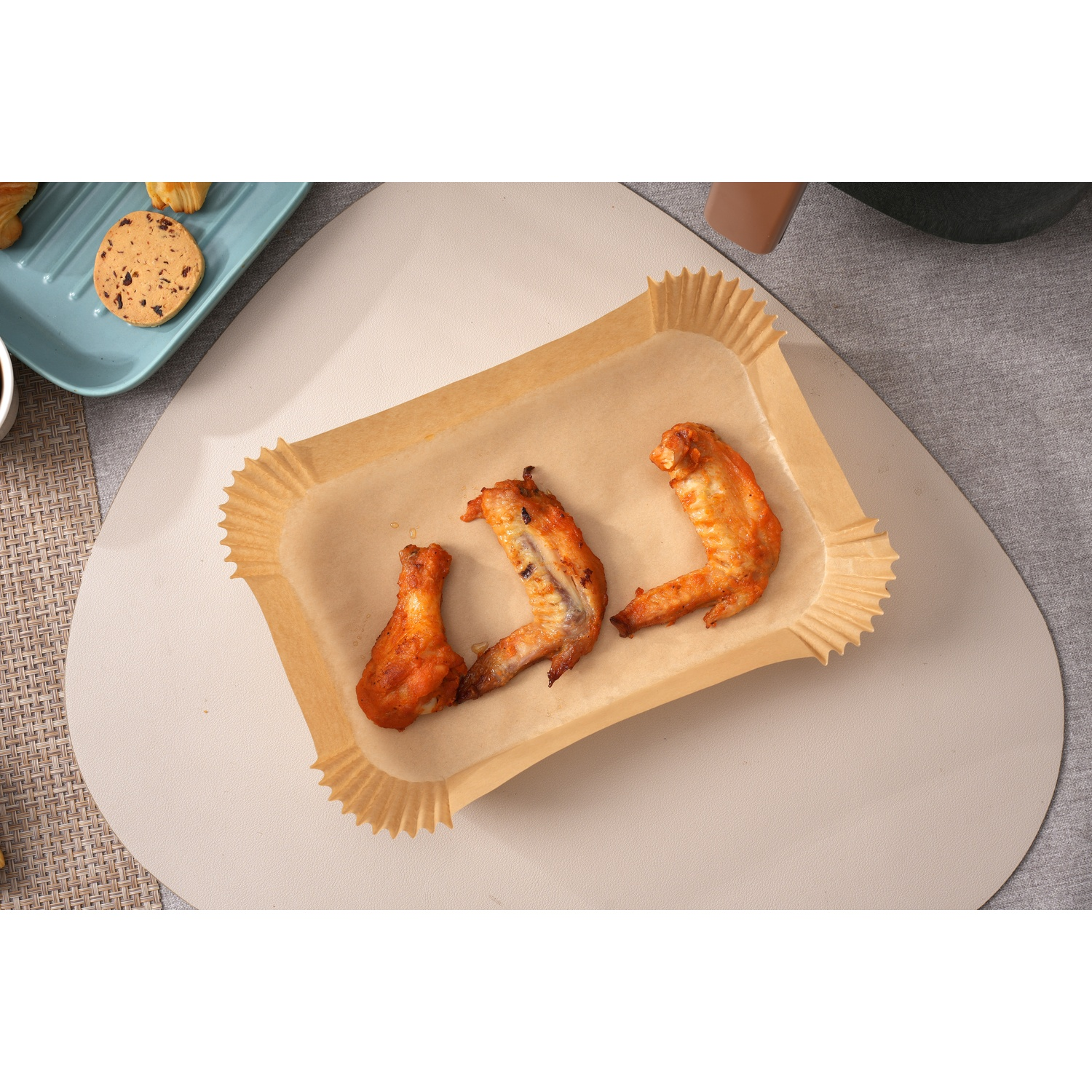 Tre ali di pollo cotte in una teglia rettangolare di carta pergamena.
