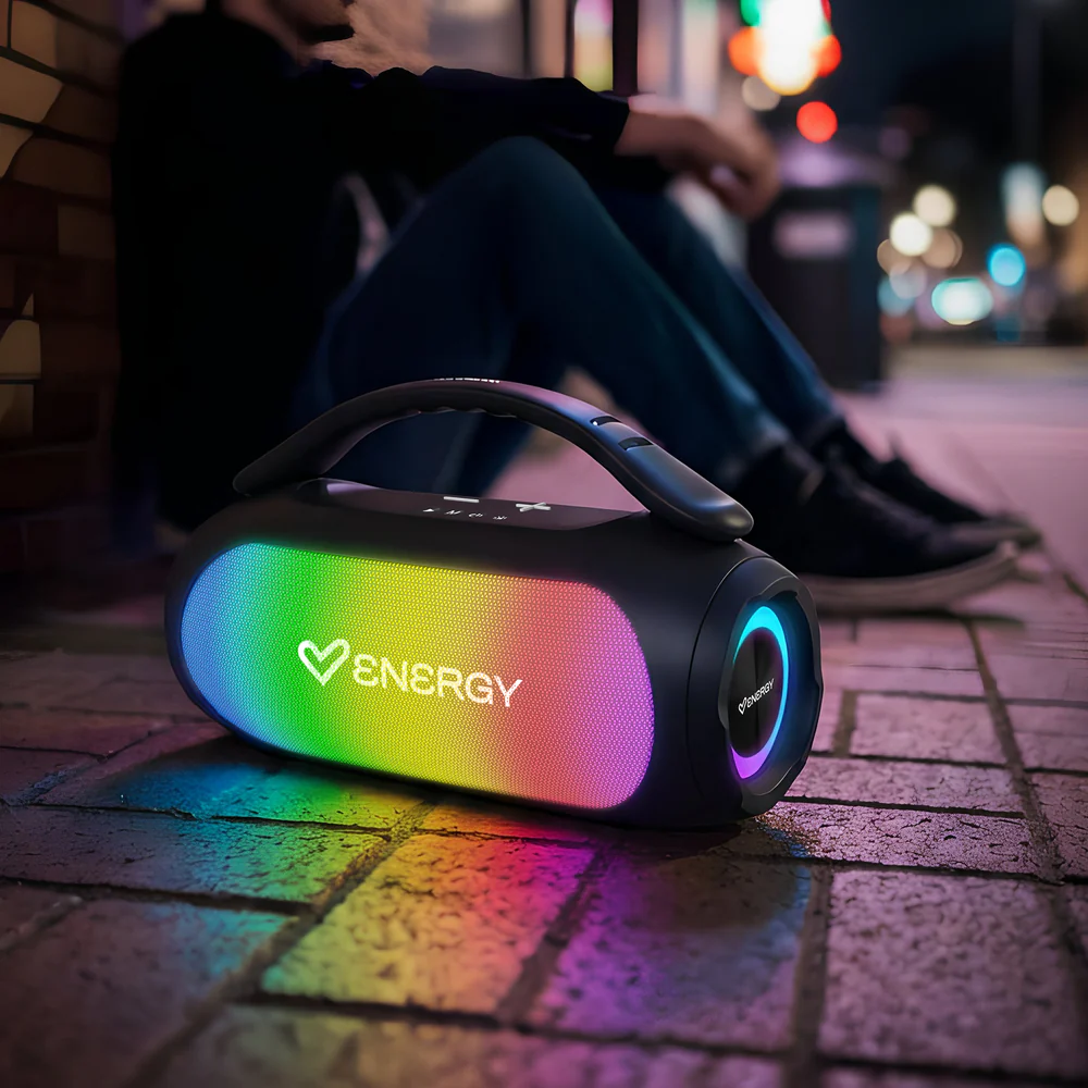 Szivárványfényes hordozható hangszóró ül a macskaköveken, háttérben egy ember ül.
