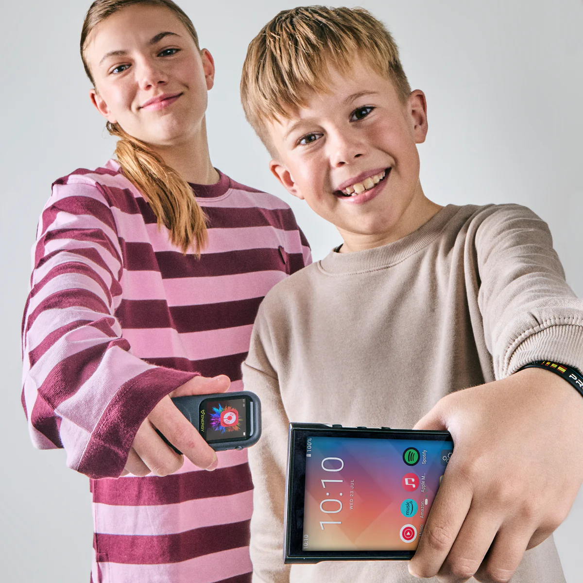 Két gyerek kütyüt tart a kezében. Egy lány rózsaszín csíkos felsőben és egy fiú barna pulóverben.