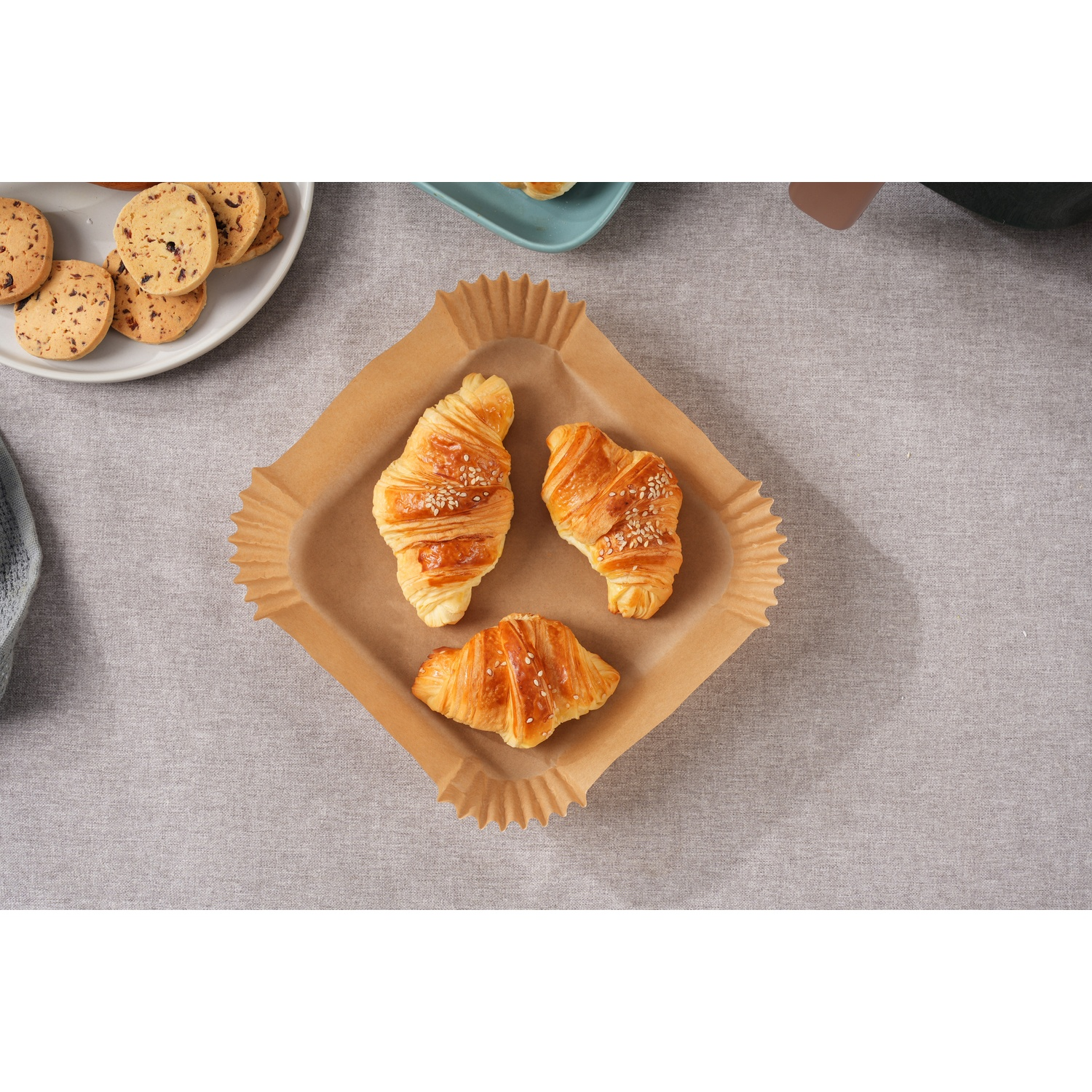 Tre croissant dorati con sesamo su carta da forno marrone, vicino ai biscotti.