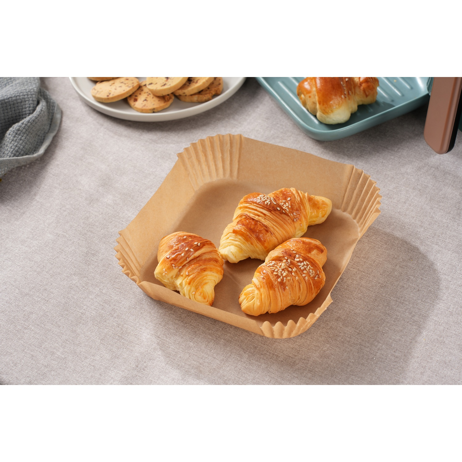 Tre croissant al sesamo in una coppetta da forno marrone, con biscotti e un dolce nelle vicinanze.