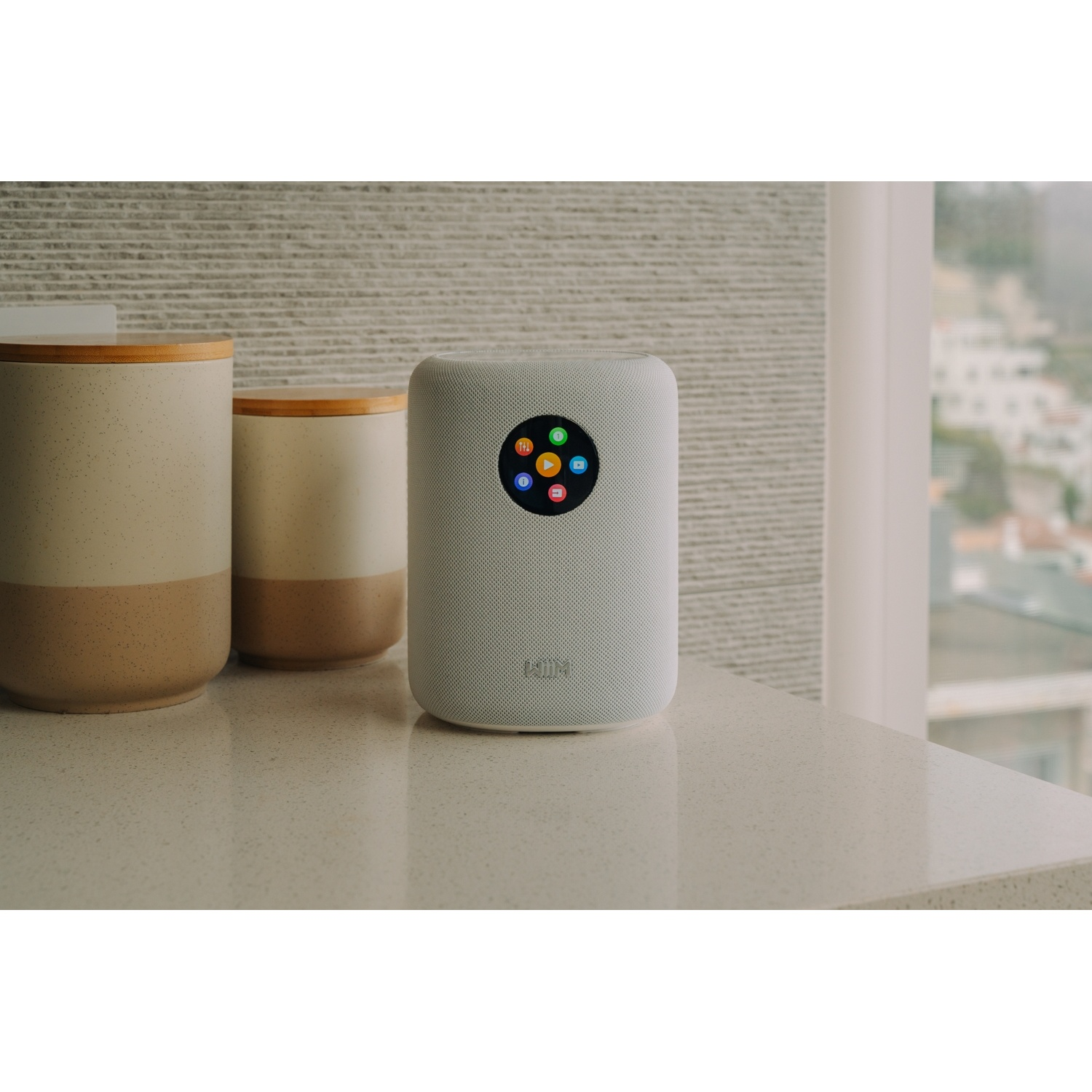 Un altoparlante bianco con icone colorate siede accanto a due contenitori su un bancone.
