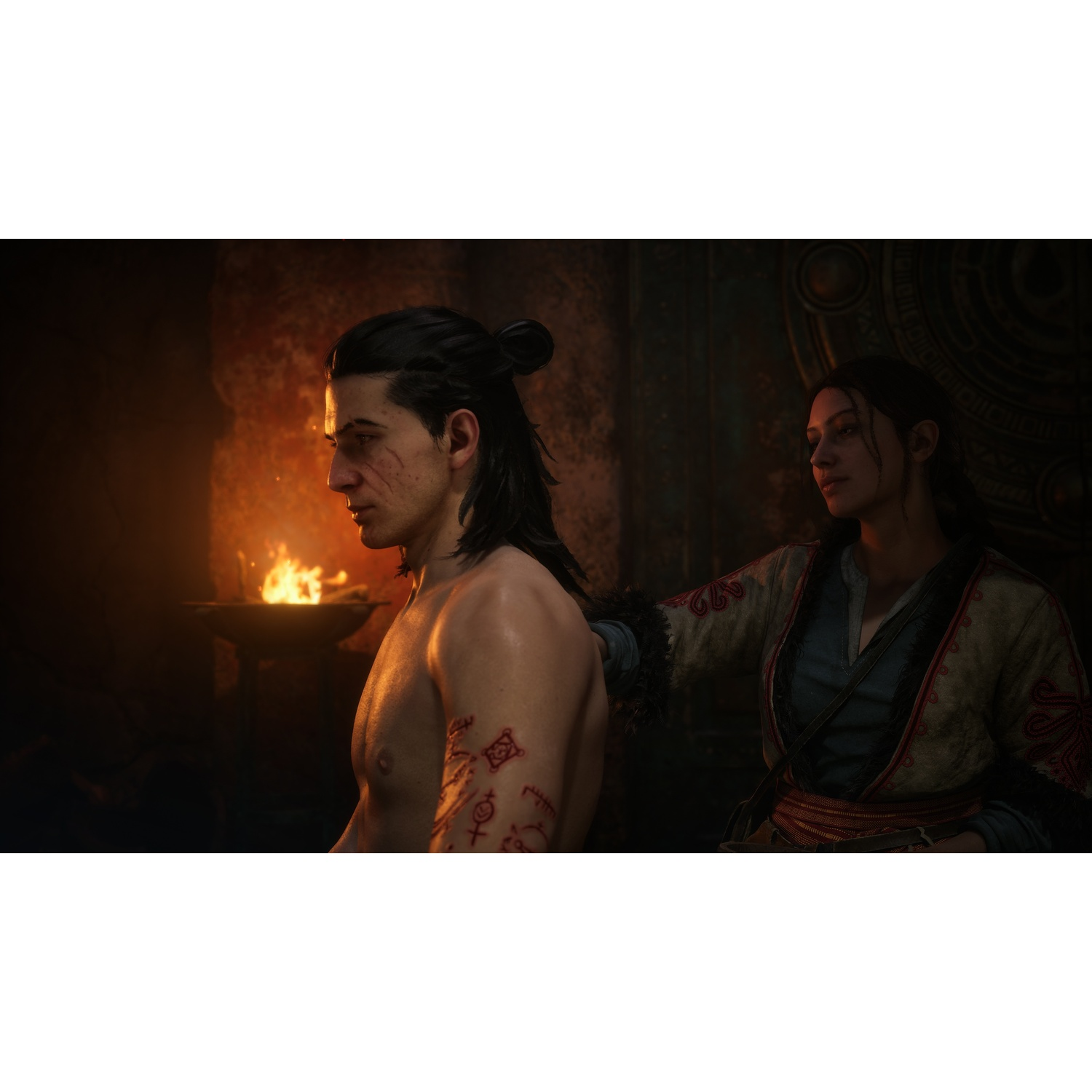 A man with tribal tattoos and a woman in traditional clothing stand near a fire.