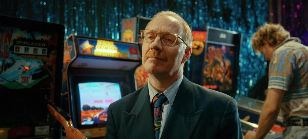 Ein Mann im Anzug blickt nach links, umgeben von Arcade-Automaten.
