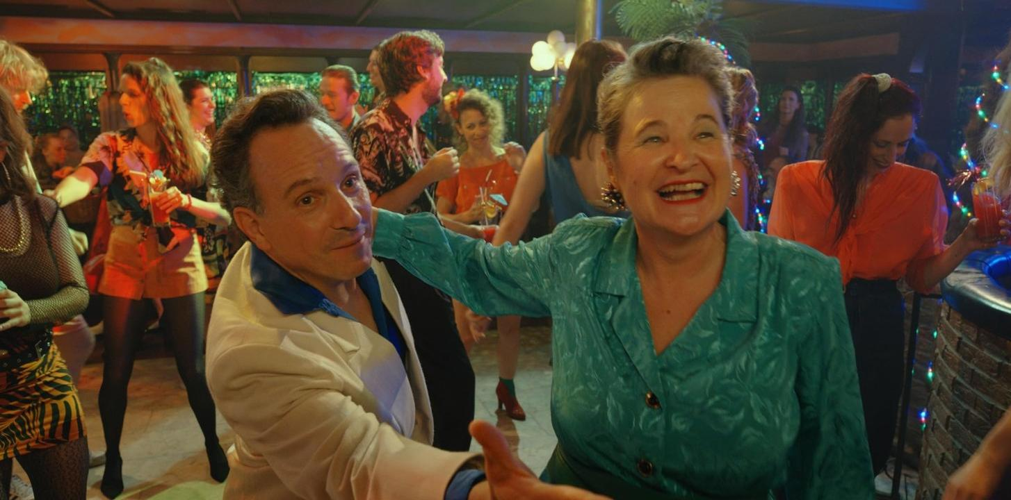 Ein Mann und eine Frau tanzen auf einer Party. Viele Leute im Hintergrund.