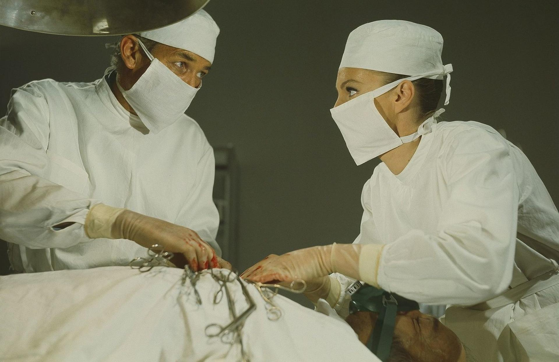 Chirurgen in OP-Kleidung und Masken operieren einen Patienten unter einem Licht.