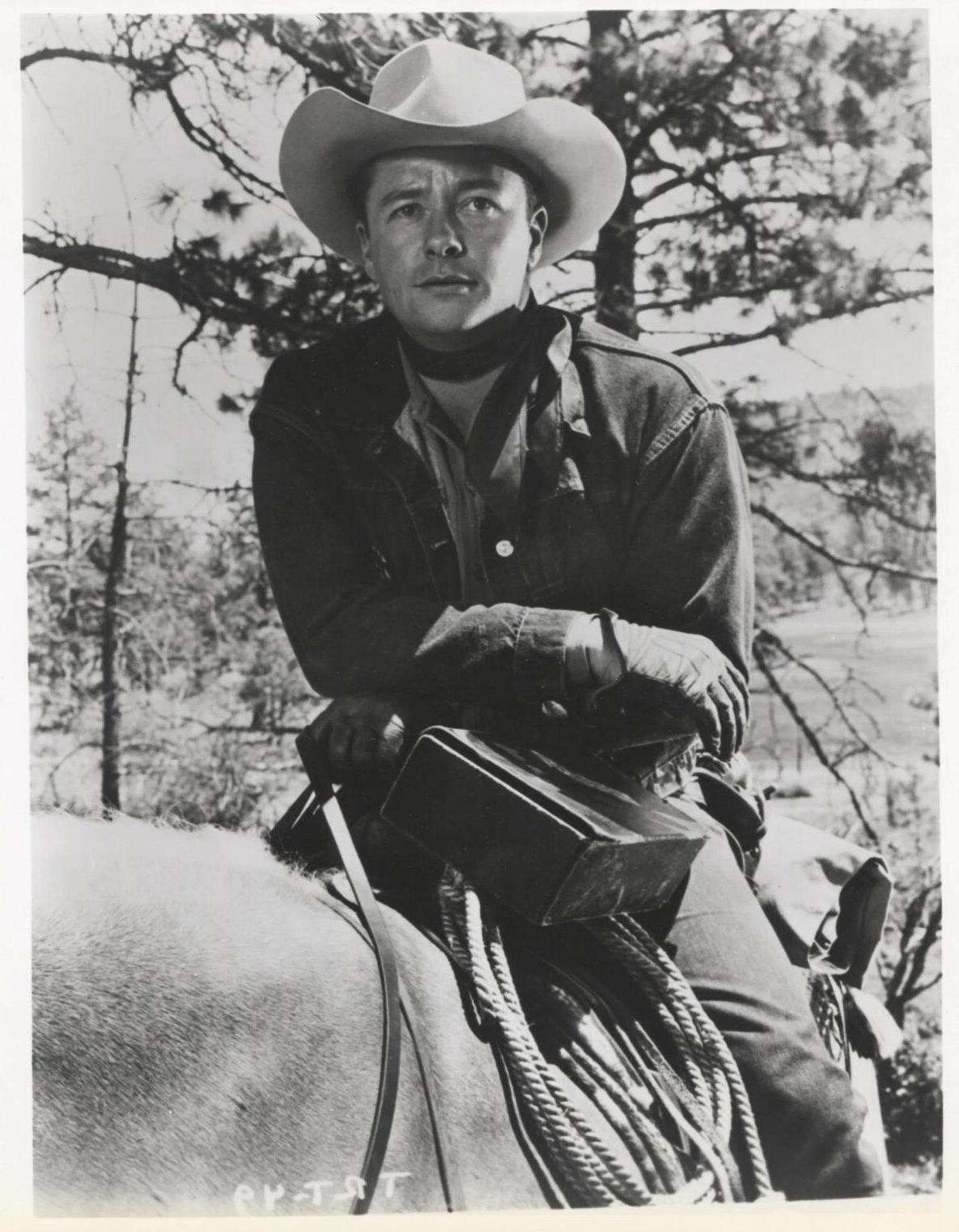 Ein Mann in einem Cowboyhut sitzt auf einem Pferd im Freien.