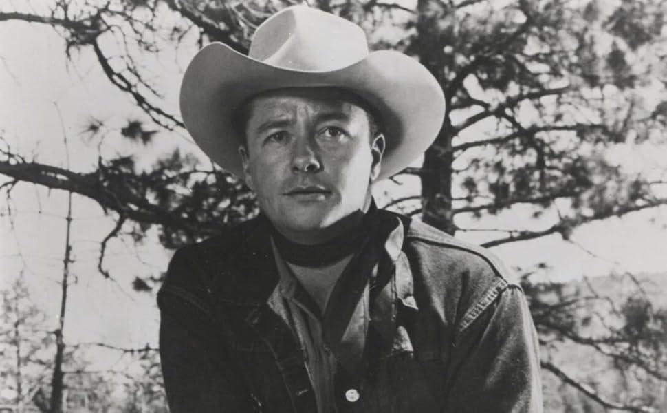 Ein Mann in einem Cowboyhut und Jeansjacke, vor Bäumen im Freien.