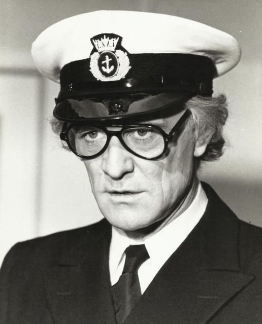 Ein Mann in Uniform mit Hut und Brille, ernster Blick.