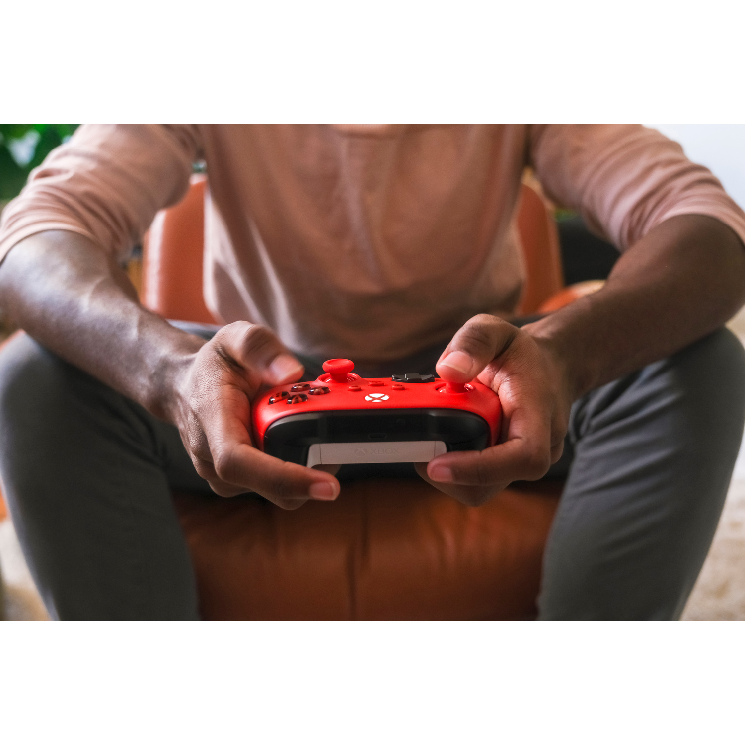 Una persona tiene in mano un controller Xbox rosso seduta su una sedia marrone.