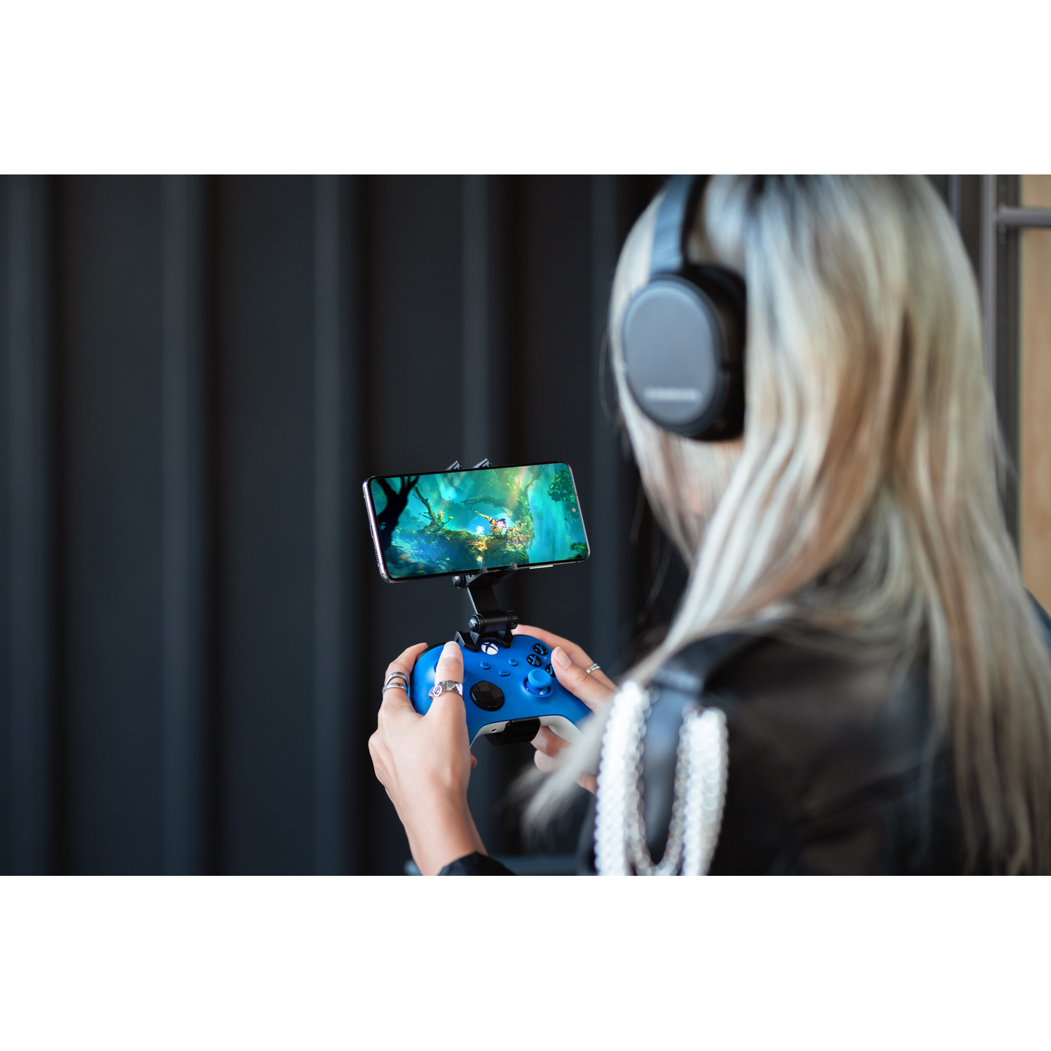 Controller blu con telefono che mostra un gioco e cuffie su una persona