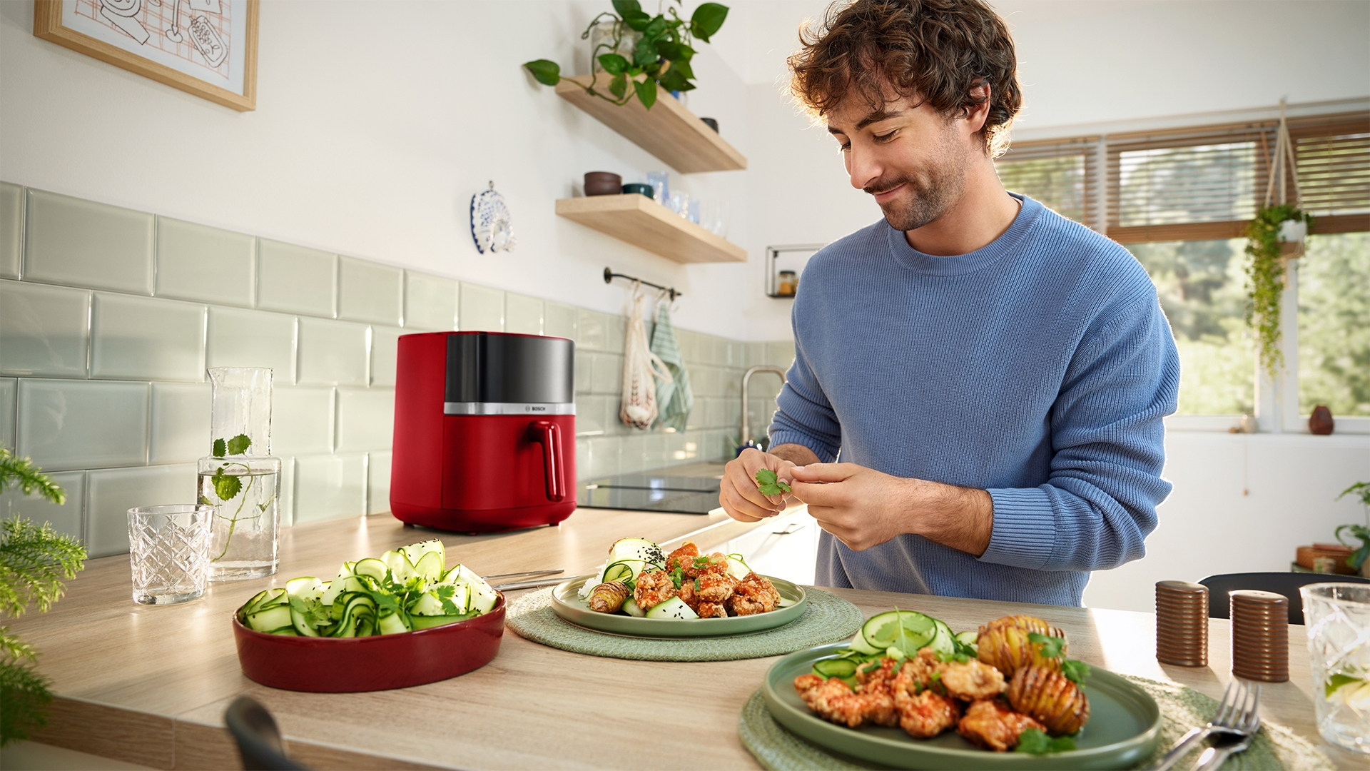 Mann garniert Essen in der Küche mit rotem Airfryer und Gurkensalat.
