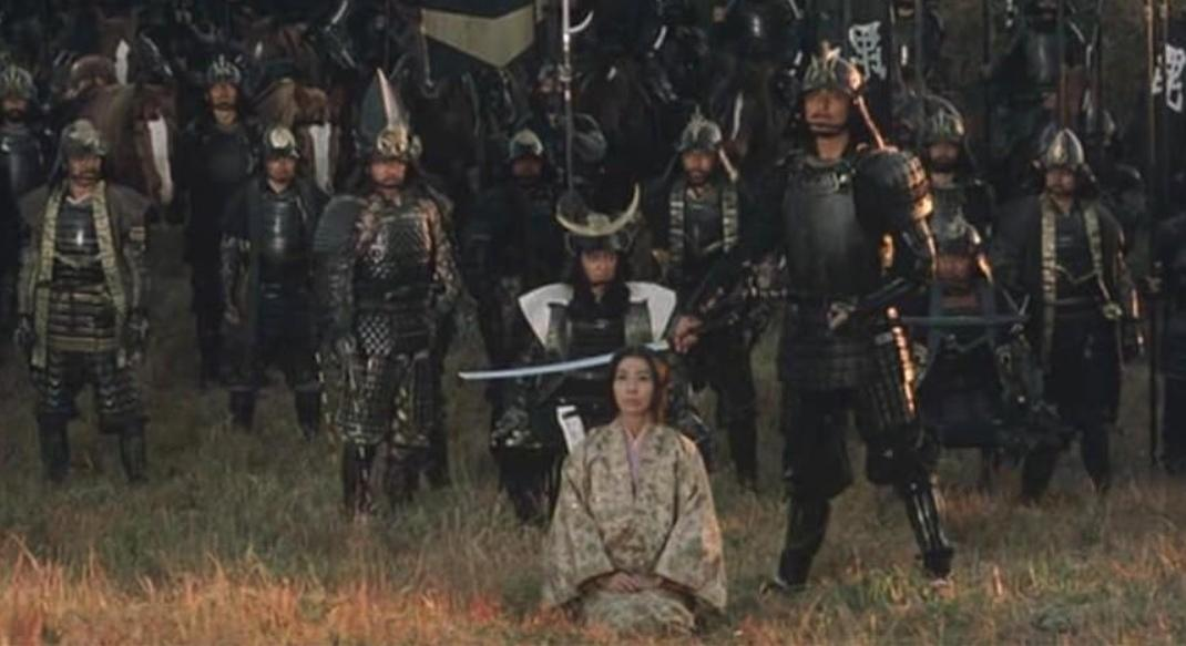Eine Frau in einem Kimono kniet vor einer großen Gruppe von Samurai-Kriegern in Rüstung.