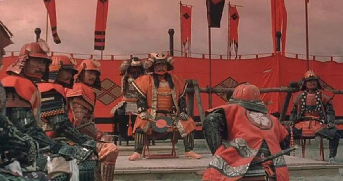 Samurai-Krieger in Rüstung sitzen vor roten Fahnen und Zelten.