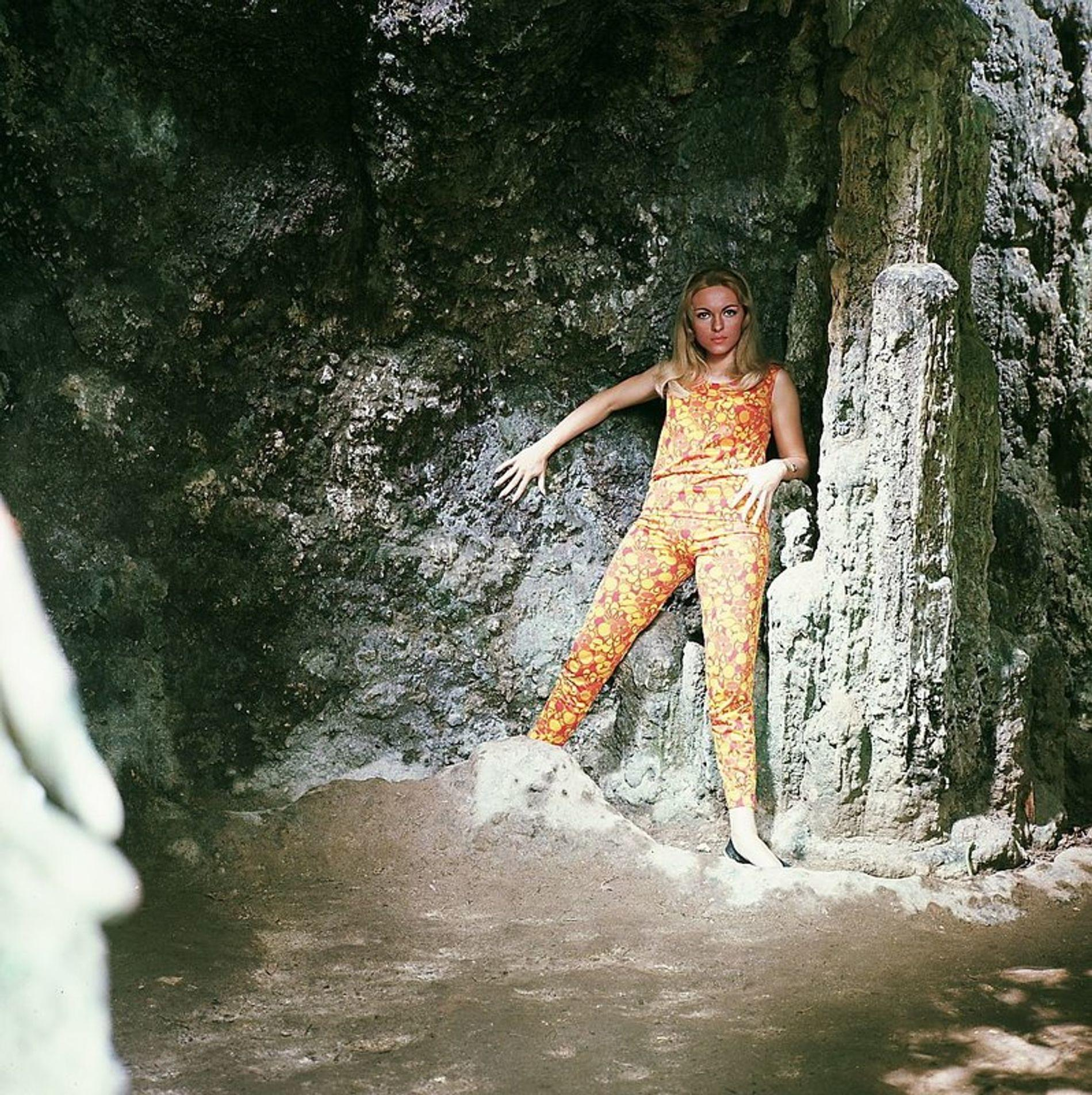 Eine Frau in orange-gelber Kleidung steht in einer Felsnische.