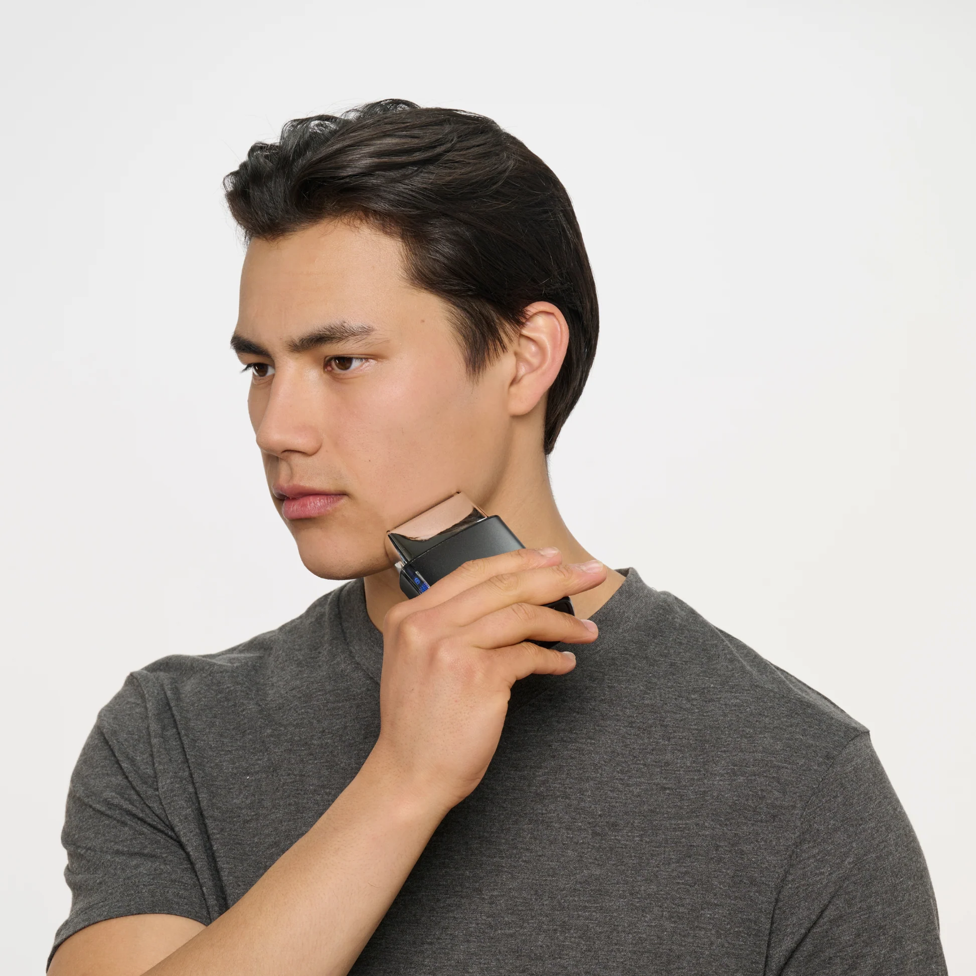 Ein Mann mit dunklem Haar rasiert sich mit einem kleinen schwarzen Trimmer den Hals.