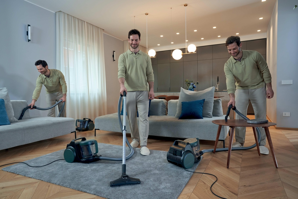 Mann saugt Couch, Teppich und Tisch in modernem Wohnzimmer.