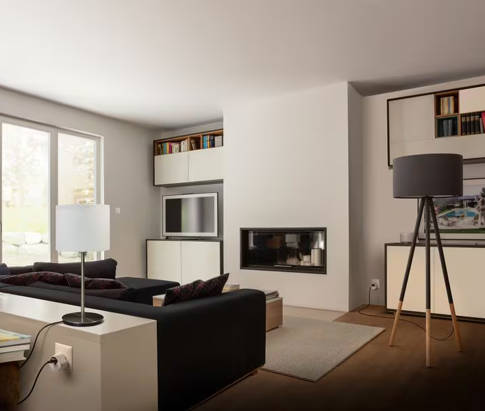Ein Wohnzimmer mit schwarzem Sofa, Tischlampe, Kamin und Stehlampe.