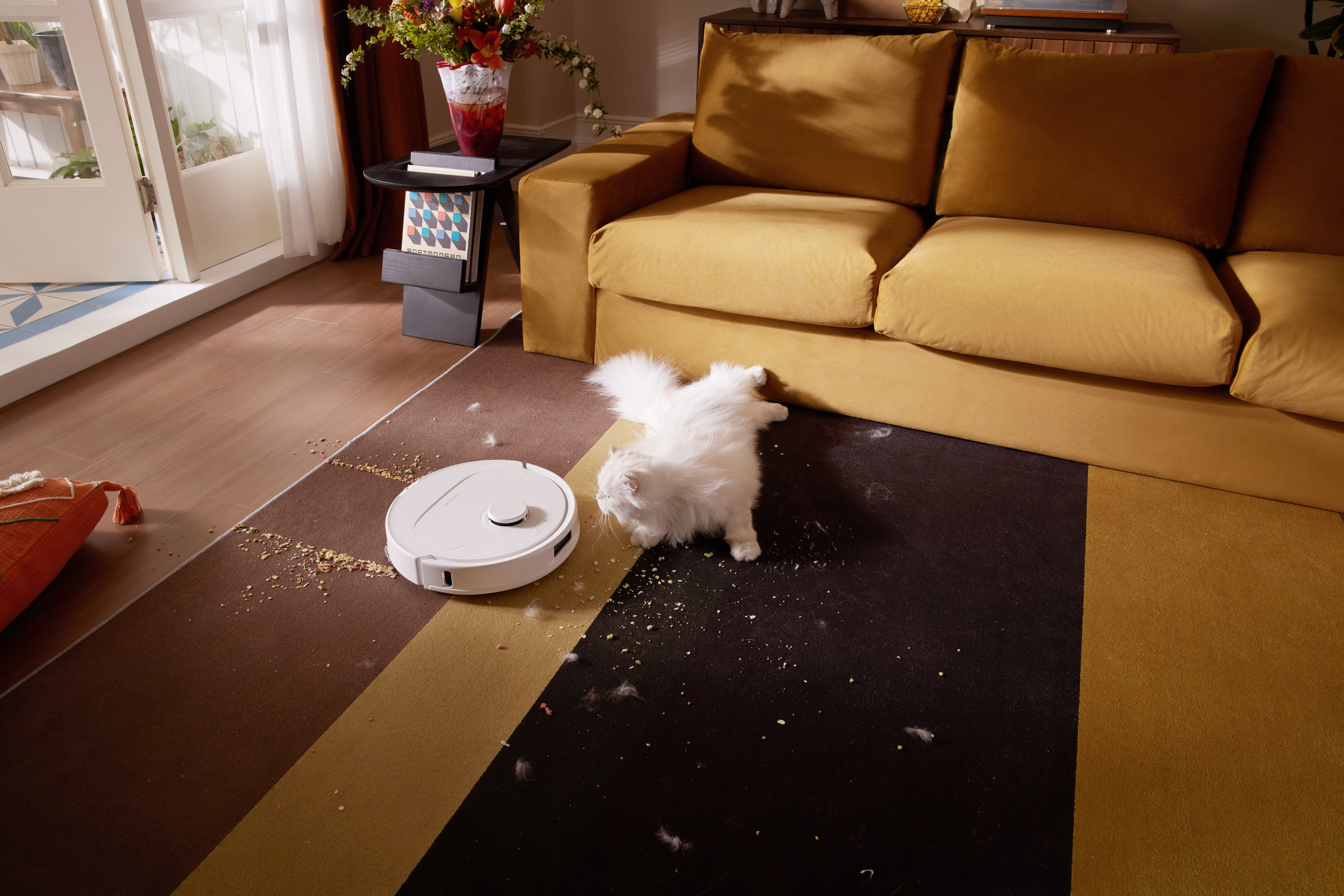 Ein weißer Saugroboter reinigt einen Teppich, auf dem eine weiße Katze liegt.