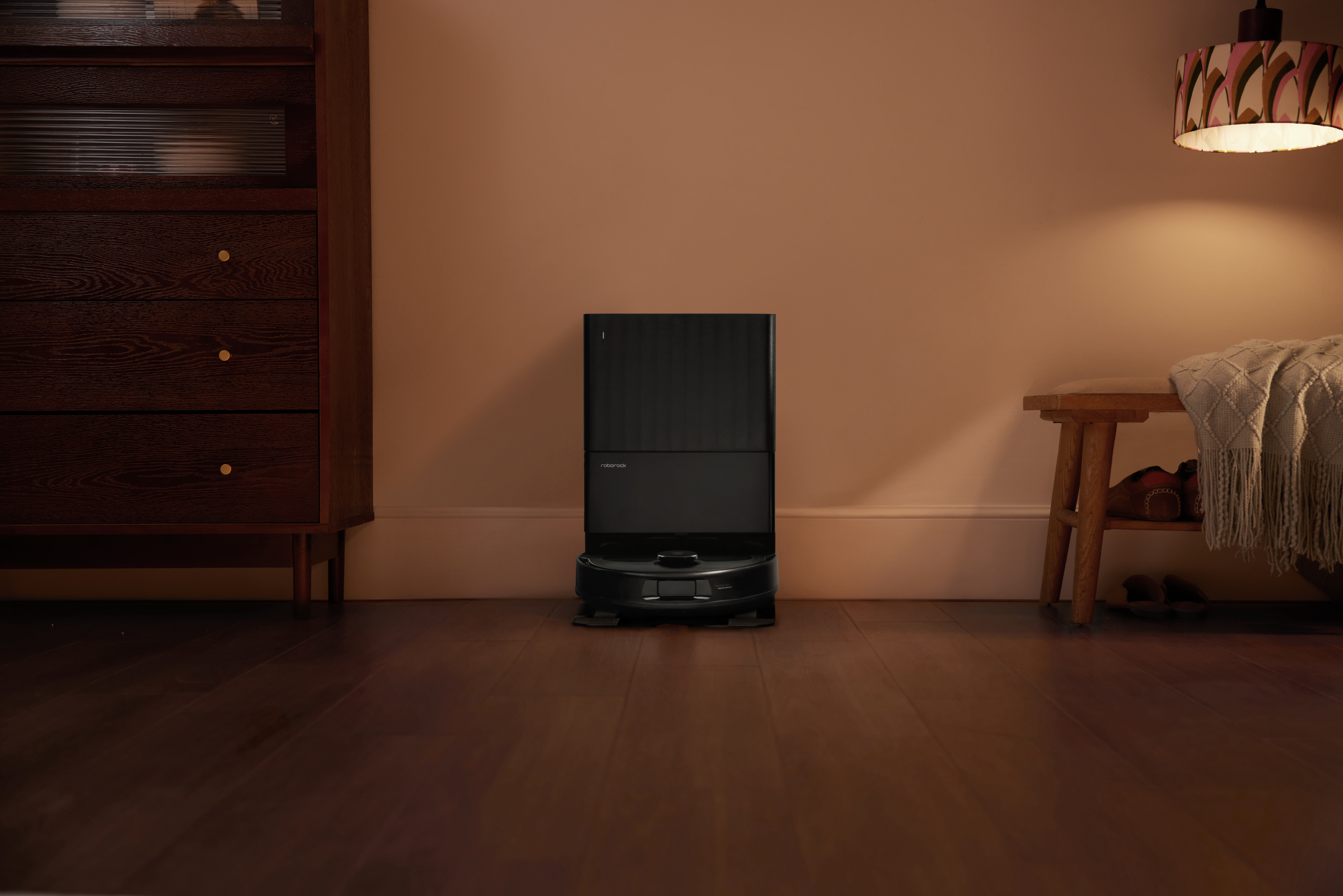 Un robot aspirapolvere nero si trova su un pavimento in legno davanti a un muro.