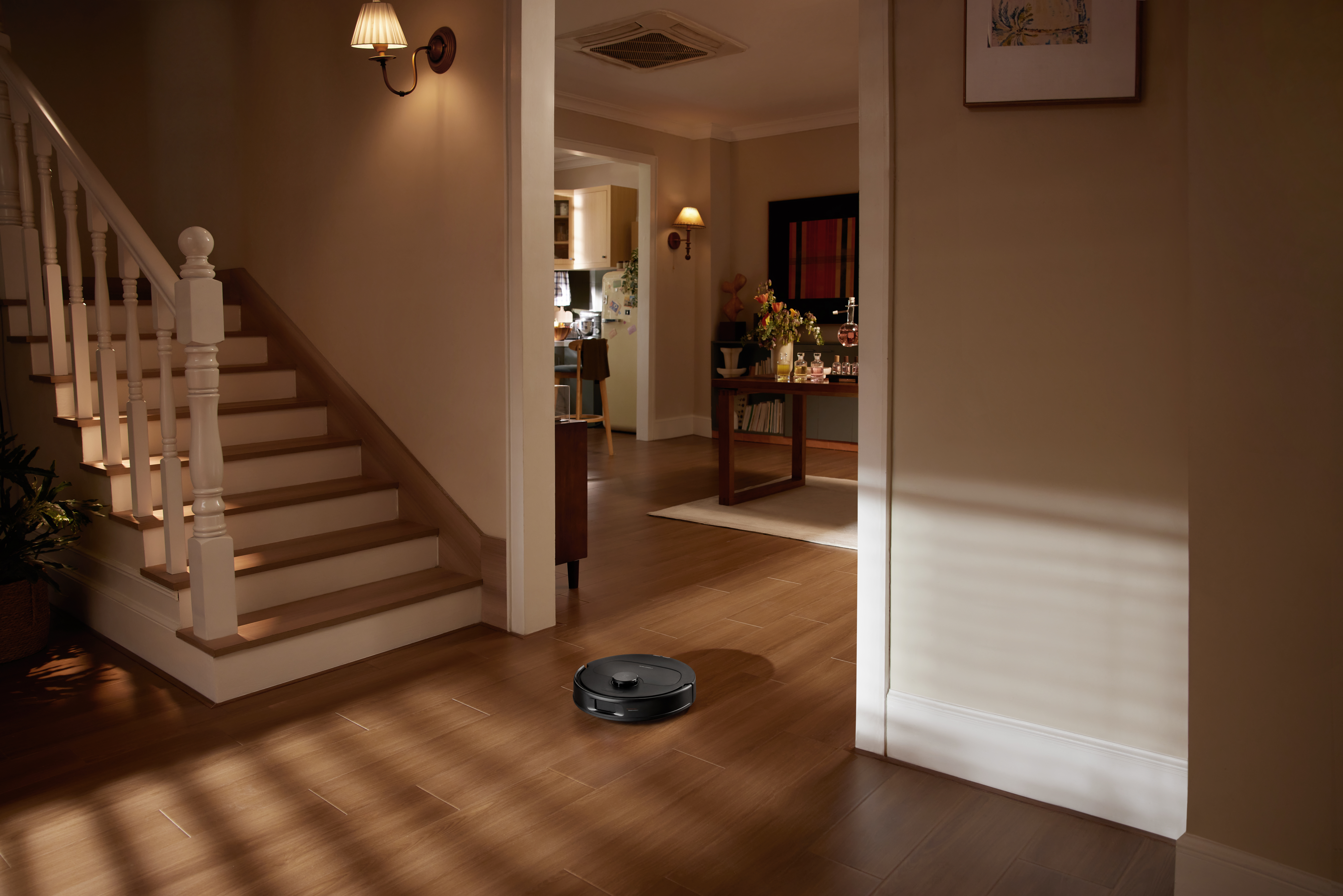Un robot aspirapolvere nero su pavimento in legno vicino a una scala.