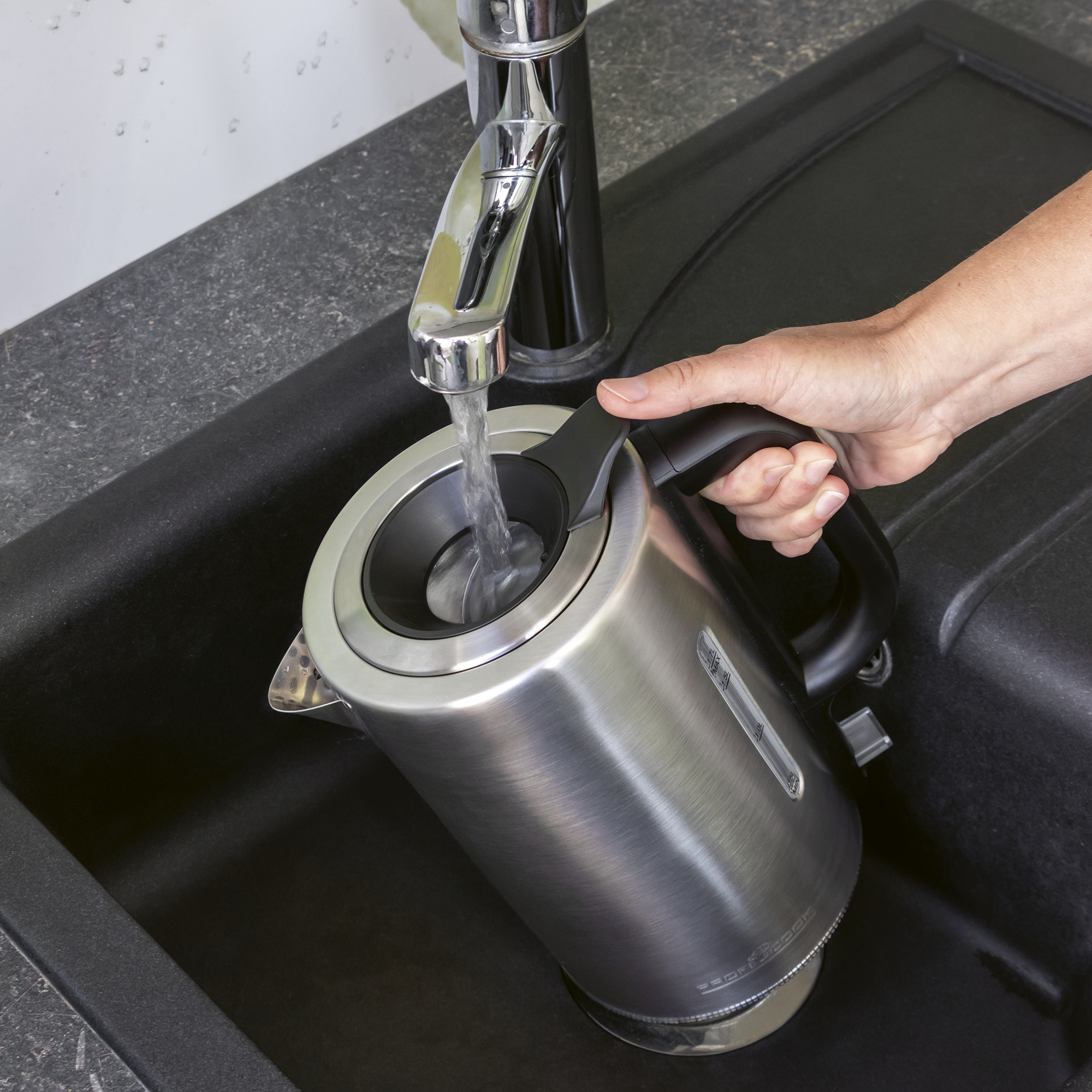 Eine Hand füllt einen Wasserkocher unter einem Wasserhahn in einer Spüle.