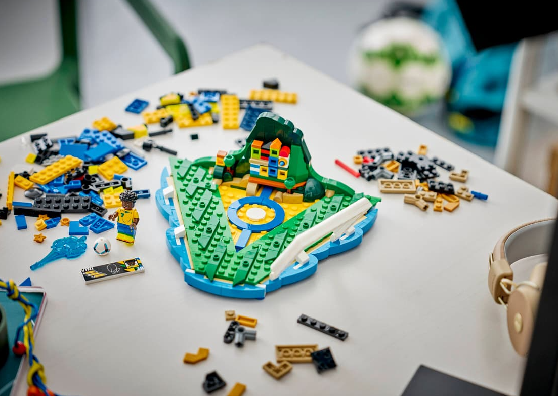 Ein Lego-Fußballstadion-Modell mit losen Steinen und einer Minifigur auf einem Tisch.