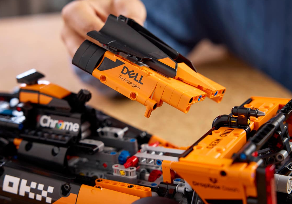 Eine Person baut einen orangefarbenen Lego-Rennwagen mit schwarzen und weißen Aufklebern.