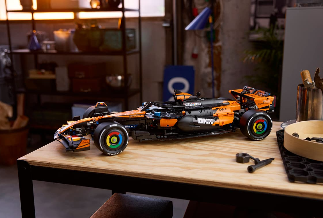 Ein detailliertes Lego-Modell eines orange-schwarzen Formel-1-Autos steht auf einem Holztisch.
