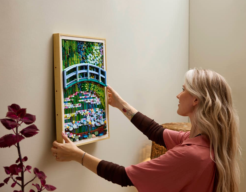Frau hängt ein gerahmtes LEGO-Kunstwerk einer japanischen Brücke und Seerosen an die Wand.