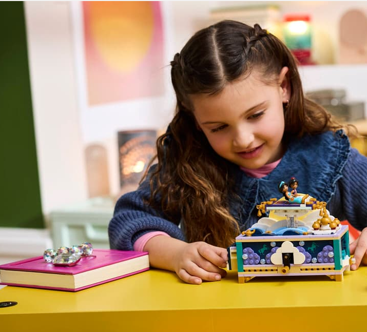 Ein Mädchen spielt mit einer bunten Lego-Spieluhr mit zwei Figuren obendrauf.