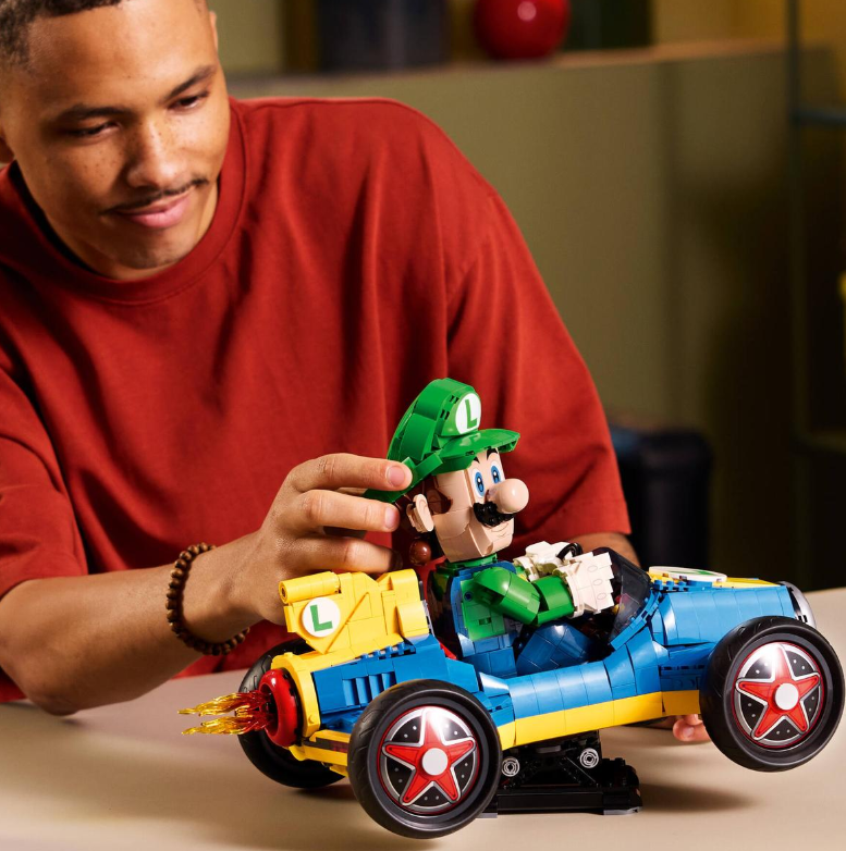 Mann mit rotem Hemd baut Lego-Auto mit Luigi-Figur.