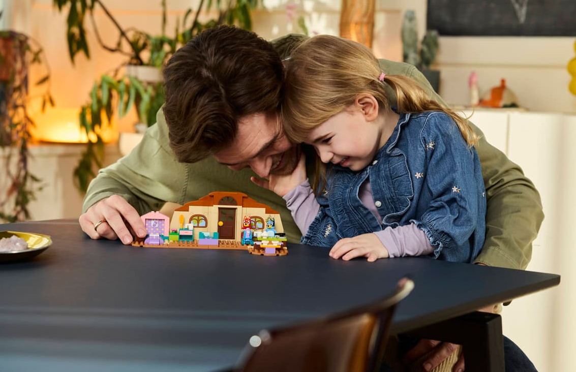 Vater und Tochter bauen Lego-Haus mit Figuren, drinnen und draußen.