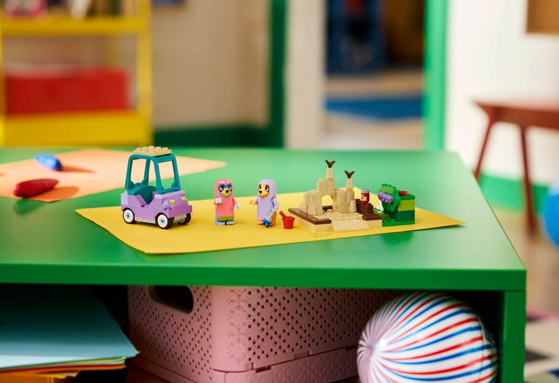 Lego-Spielzeug auf einem grünen Tisch: Auto, Figuren, Sandburg und Baum.