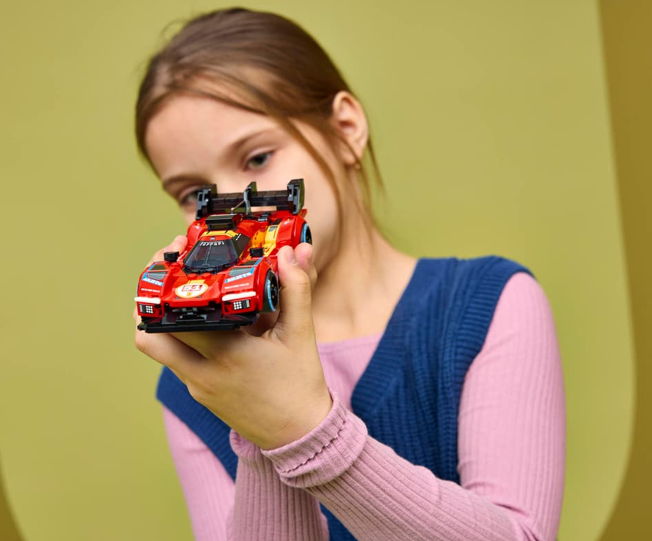 Ein Mädchen hält einen roten Spielzeugrennwagen mit Flügeln und Aufklebern.