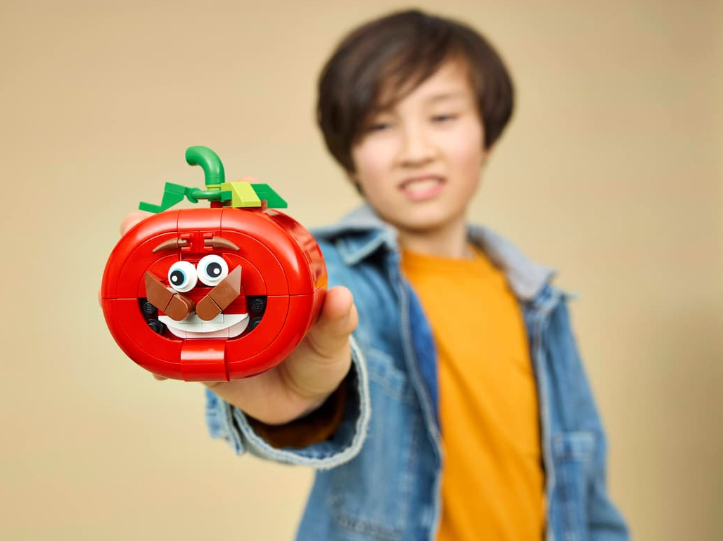 Ein Junge hält eine rote Lego-Tomate mit lustigem Gesicht vor sich.