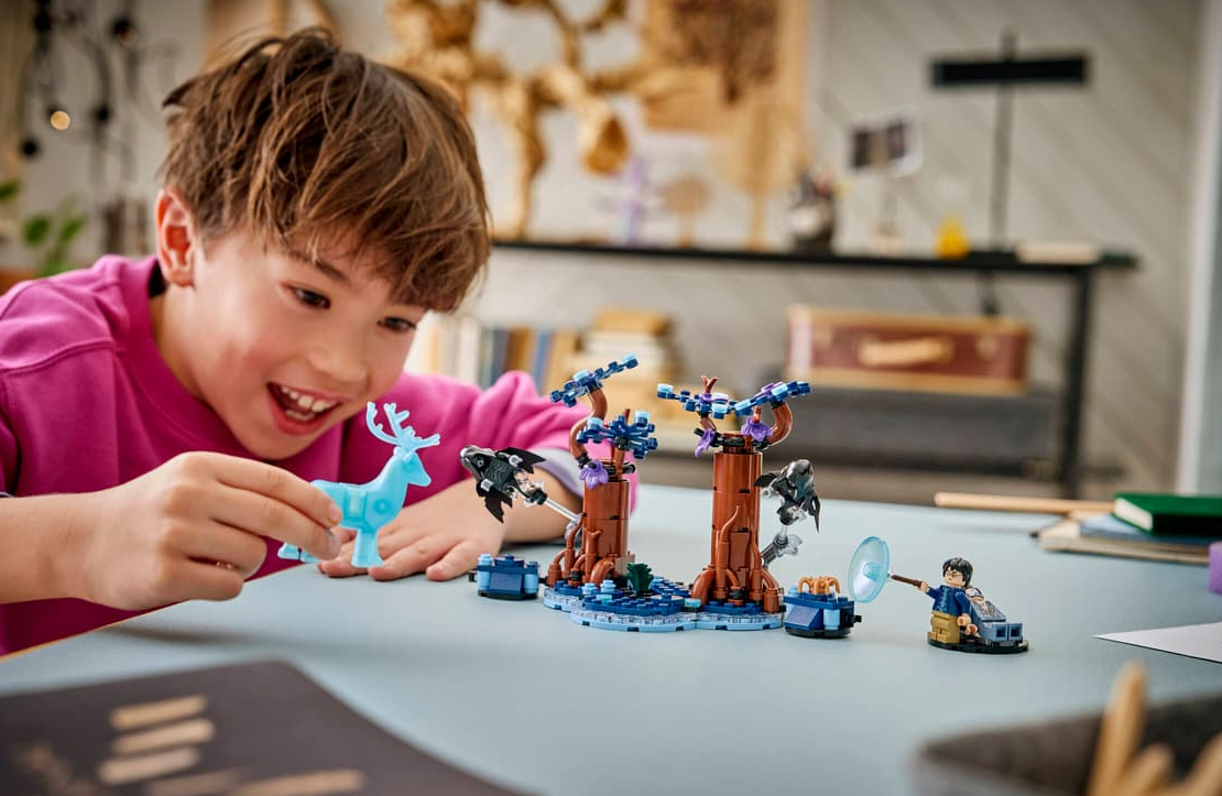 Ein Junge im pinken Hemd spielt mit einer blauen Hirschfigur und einem Lego-Set.