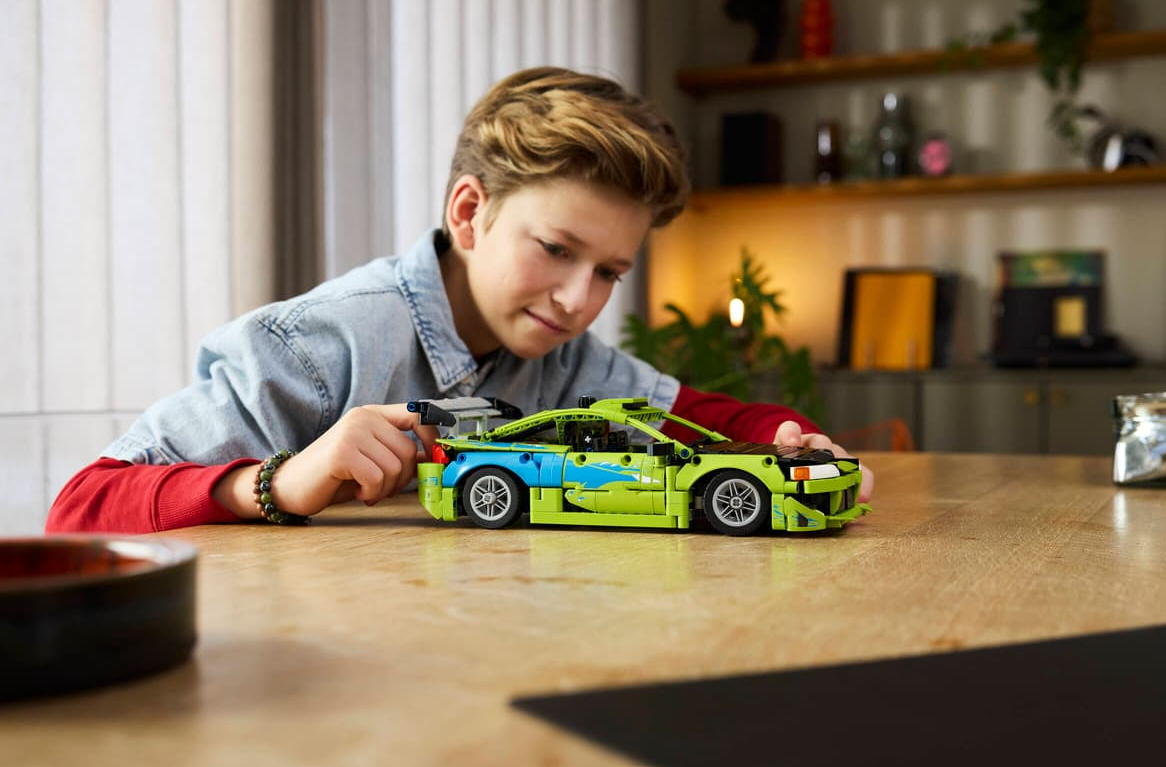 Ein Junge spielt mit einem grünen und blauen Lego-Rennwagen auf einem Holztisch.
