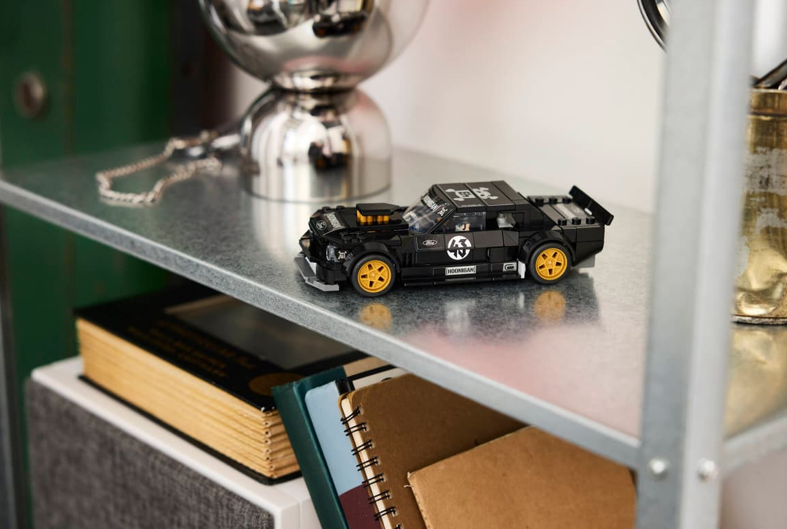 Ein schwarzer Lego-Rennwagen mit gelben Felgen steht auf einem Regal.